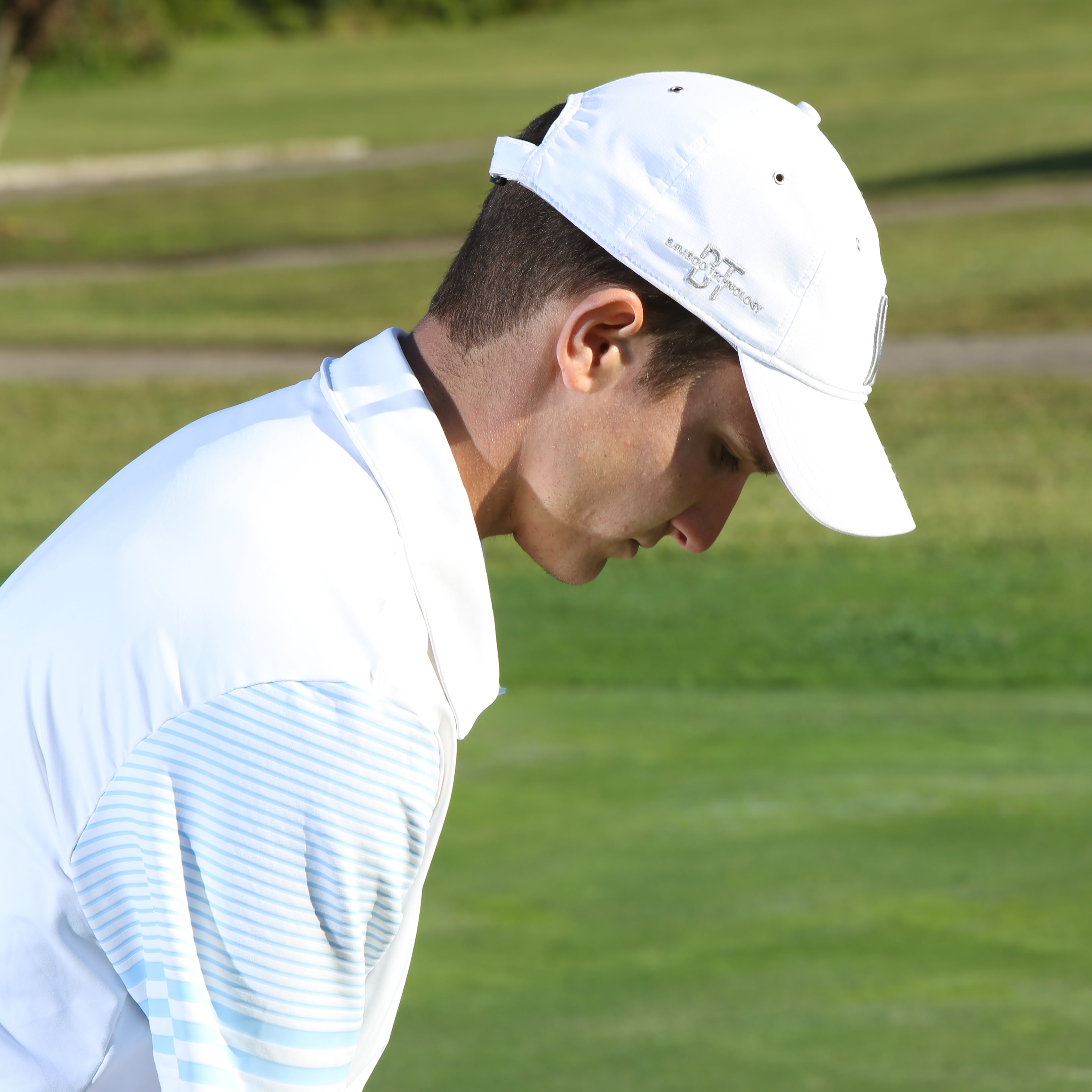 Close up of a guy wearing his golfing hat on the course.
